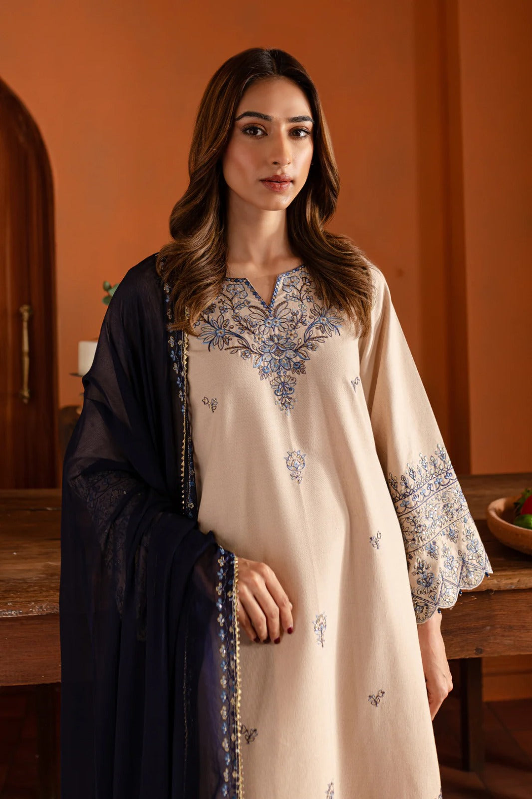 Woman wearing a beige embroidered dress with a black dupatta in an indoor setting.