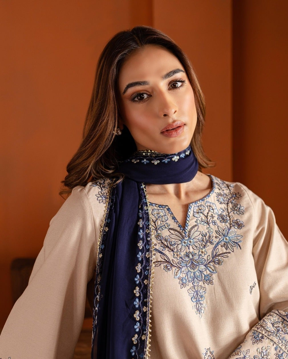 Woman wearing a beige embroidered shirt with a navy scarf against an orange background