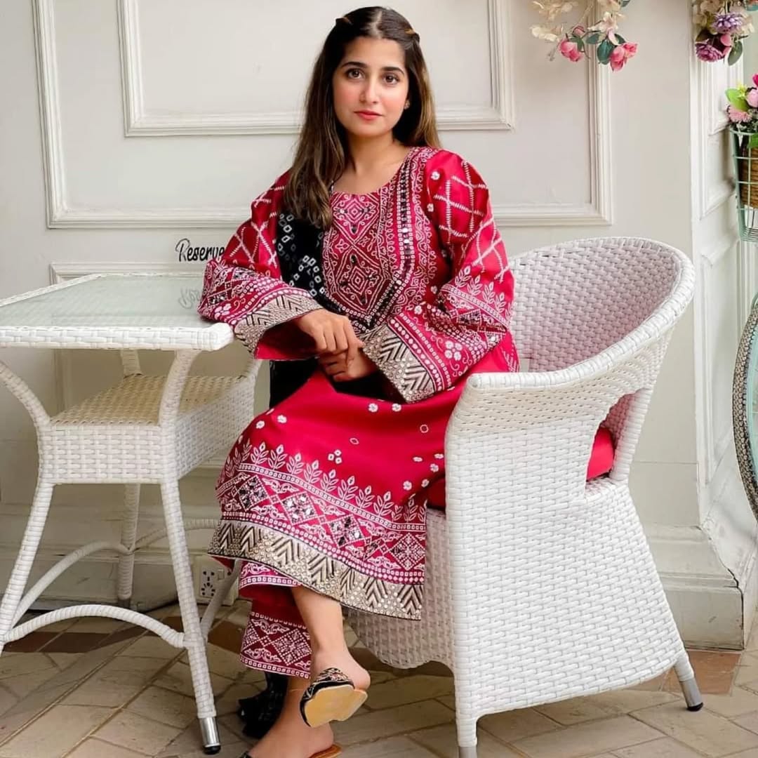 Woman in a red and patterned dress sitting on a white chair in a decorated room.