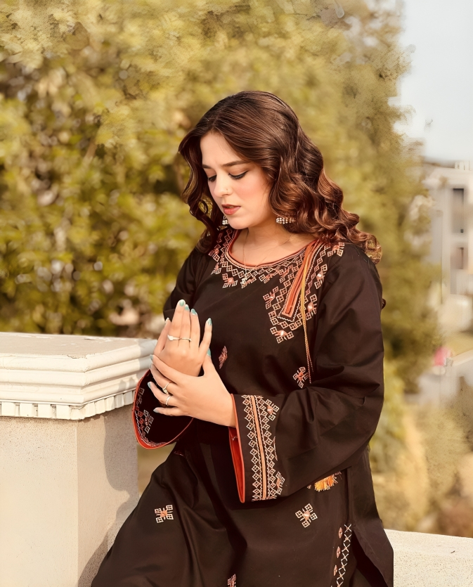 Woman wearing a black embroidered dress sitting outdoors with greenery in the background