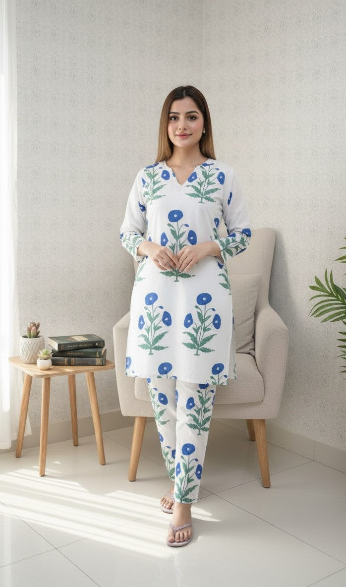 Woman wearing a floral pajama set in a bright room with a chair and small table.