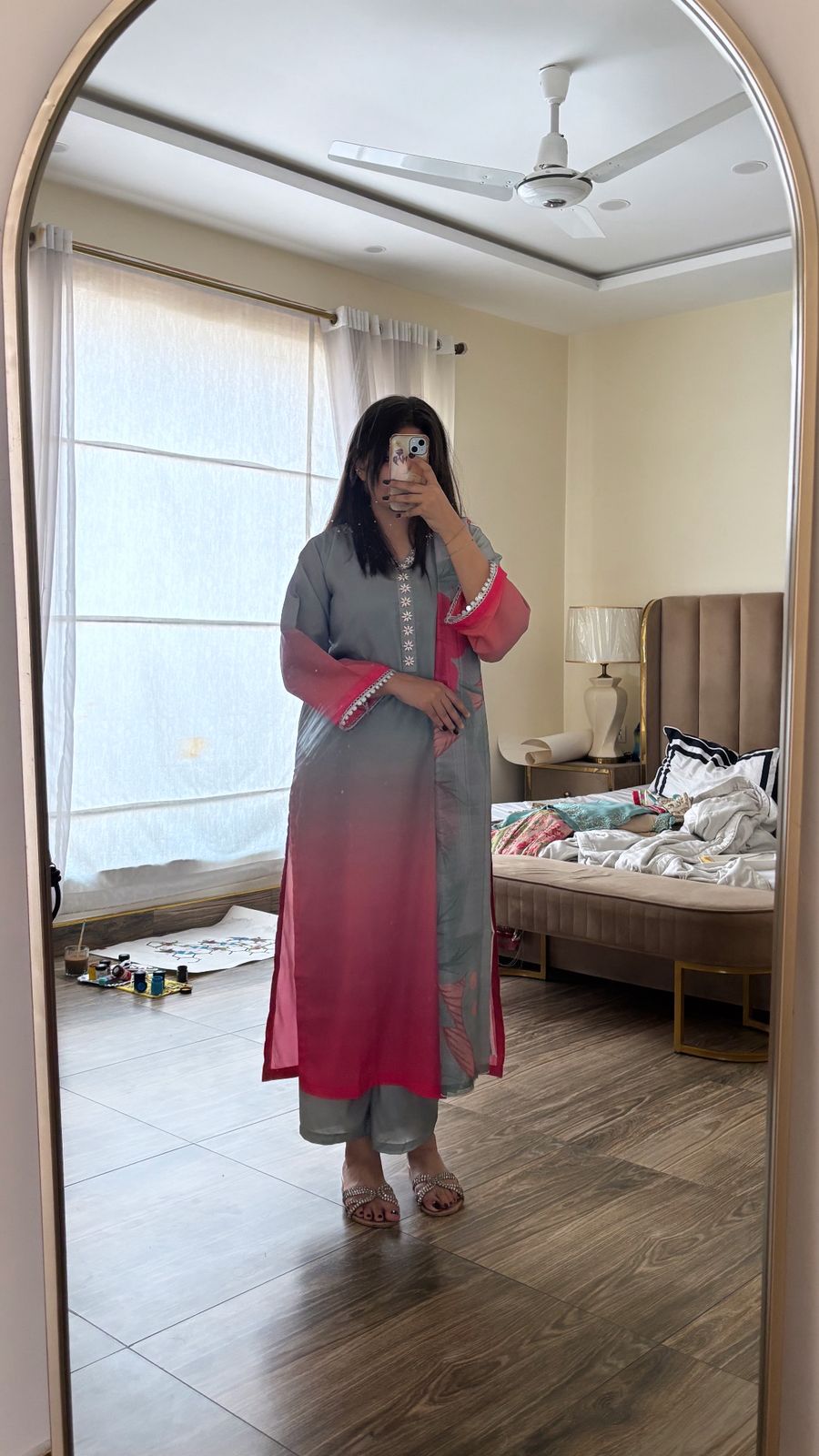 Person taking a mirror selfie wearing a pink and gray outfit in a bedroom.