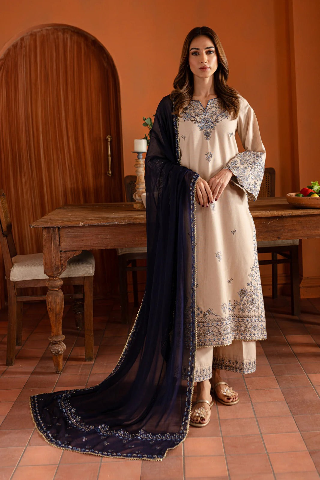 Woman in a traditional outfit with a dark blue dupatta in an indoor setting.